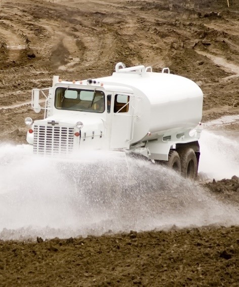 A truck pouring water on a gravely ground.